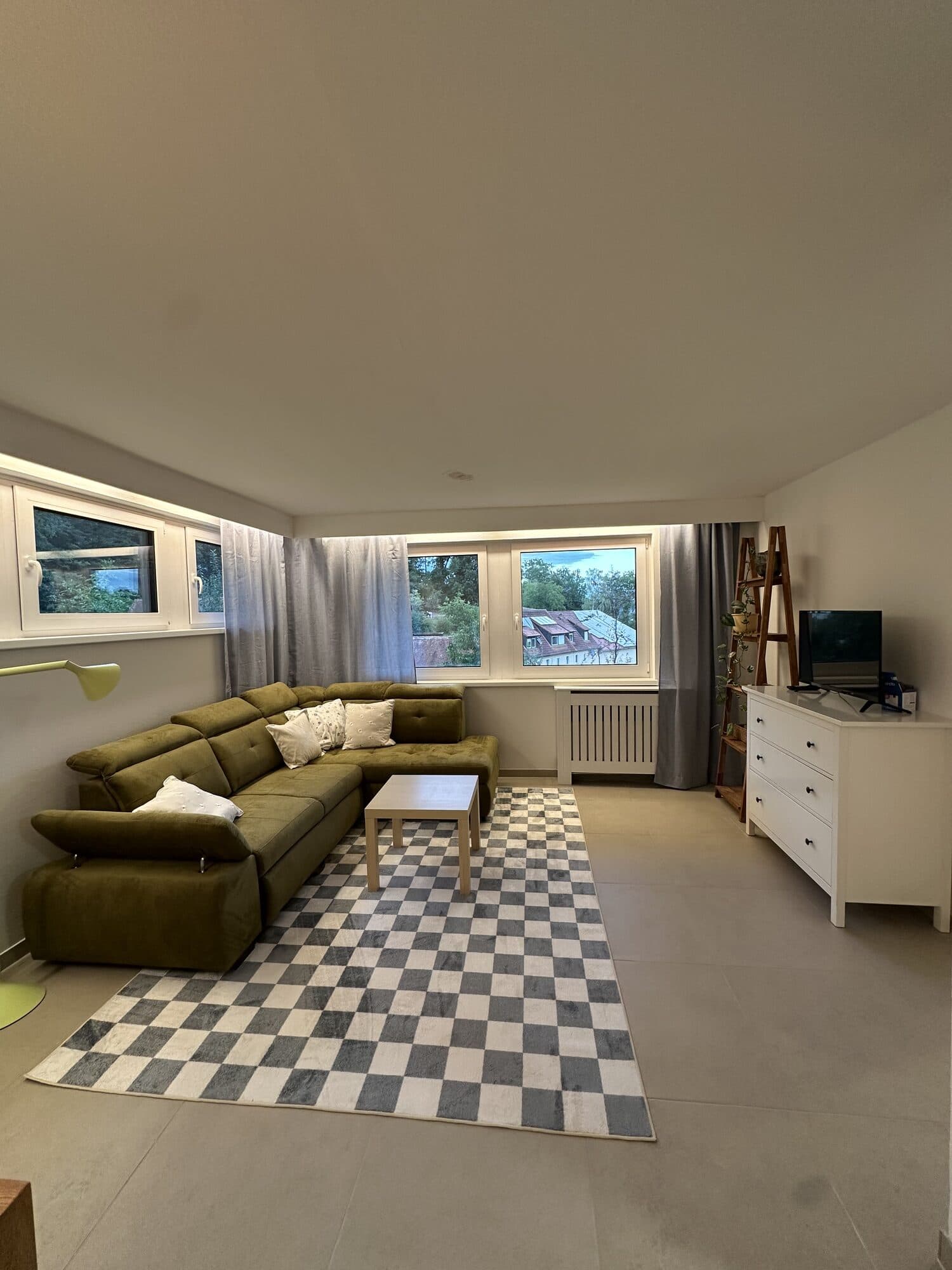 Ecksofa mit Kissen, karierter Teppich und Fernseher auf weißer Kommode